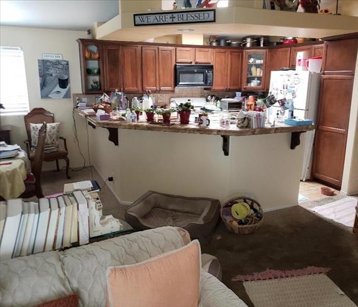 a kitchen with brown cabinets, things around the counter. Couch, dining table and a lot of small things everywhere. 