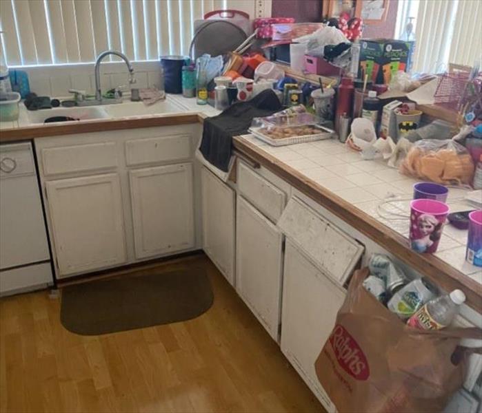 Kitchen cabinets with damaged drawers and things all over the counter tops. 