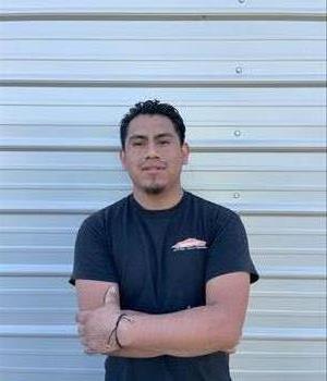 A Hispanic man with black hair and black shirt, standing with his arms crossed. 