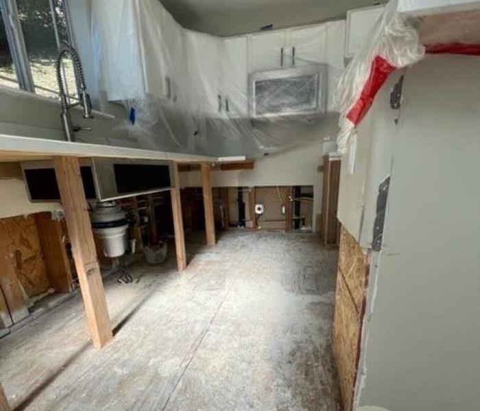 White kitchen missing lower cabinets. Floors are missing. Upper cabinets covered in plastic. 